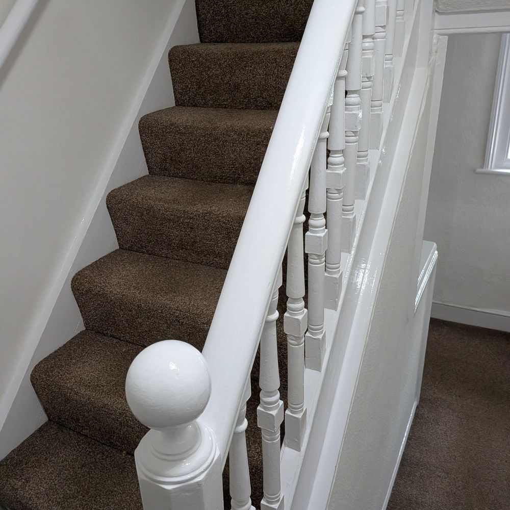 Carpeted staircase with freshly painted white banister and spindles, decorated by Steven