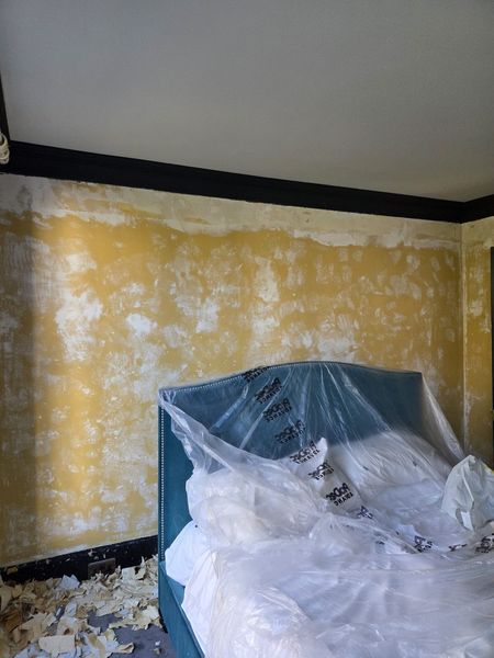 In progress: bedroom with old wallpaper stripped and the bed protected under dust sheets