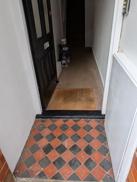 Entrance hall with freshly painted walls, skirting and door frame above a red and black tiled floor