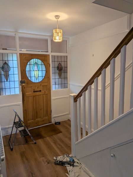 Hallway after decorating, with white walls, a white-painted staircase and the original stained-glass front door