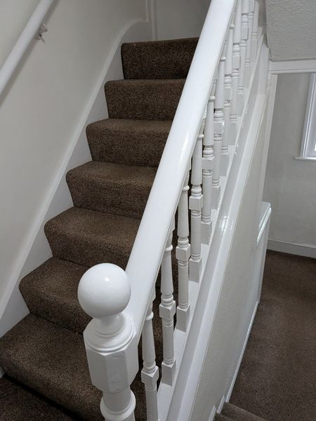 Carpeted staircase with a freshly painted white banister, spindles and round newel post