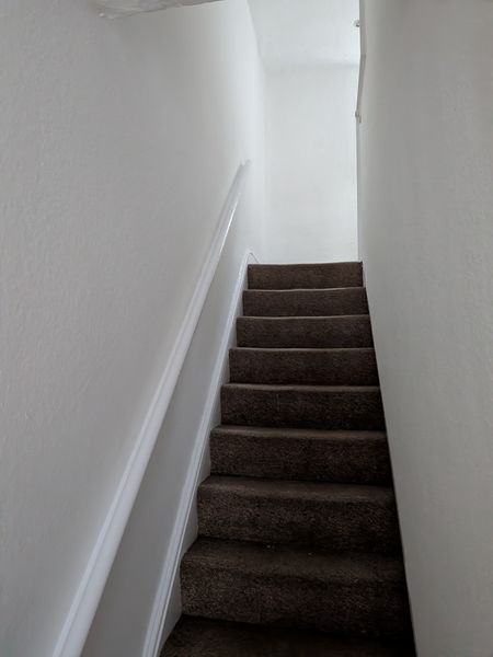 Carpeted staircase between freshly painted white walls with a white skirting