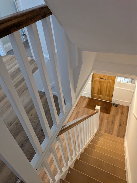 View down a freshly painted staircase with white spindles towards the front door